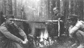 Wrzesień 1944 r., lasy koneckie. Przy ognisku od lewej: „Baca”,  „Wyżerko” (stoi), „Jerzy” i „Tudor”.